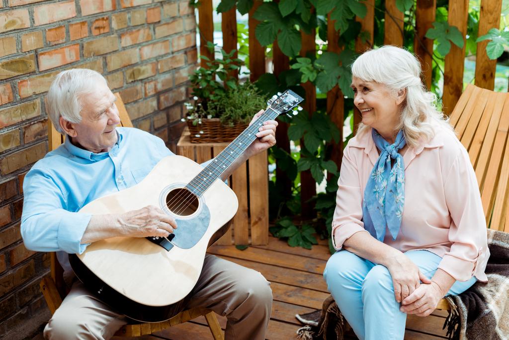 Glückliche Rentnerin schaut Ehemann beim Spielen von Akustikgitarre an  - Foto, Bild