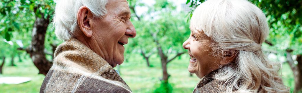 Panoramabild des älteren Ehemannes, der die glückliche Rentnerin in karierter Decke betrachtet  - Foto, Bild