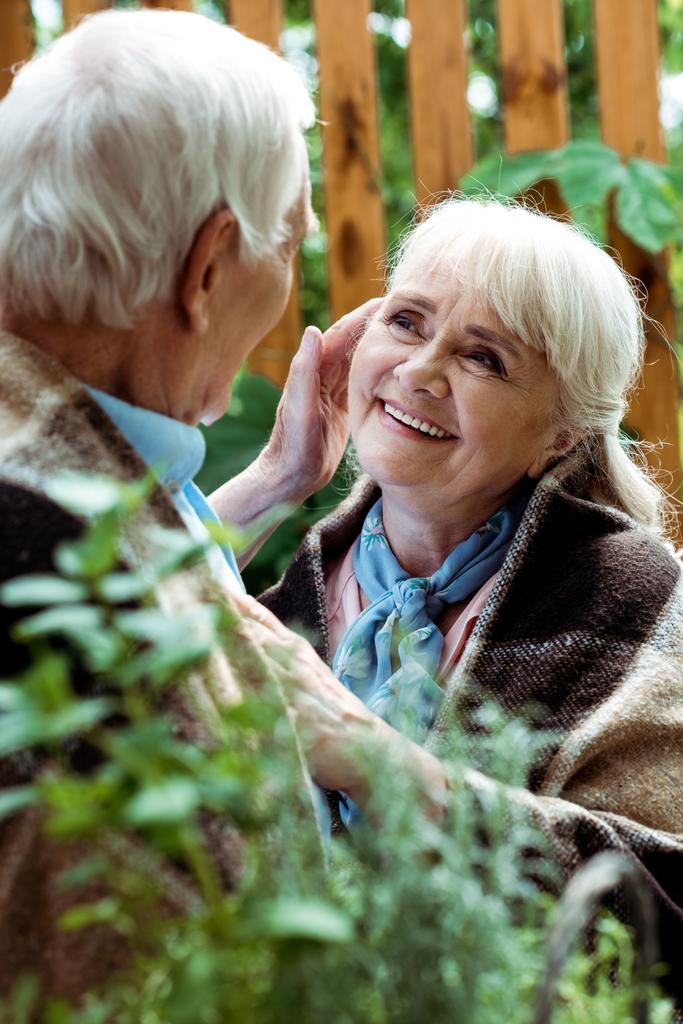 επιλεκτική εστίαση της ευτυχωμένης γυναίκας με γκρίζα μαλλιά κοιτάζοντας συνταξιούχο σύζυγο  - Φωτογραφία, εικόνα