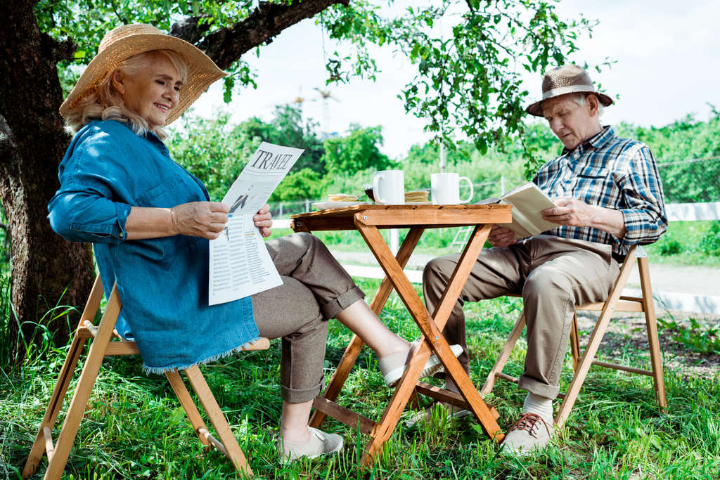 Senior vrouw lezing reizen krant in de buurt van echtgenoot met boek  - Foto, afbeelding
