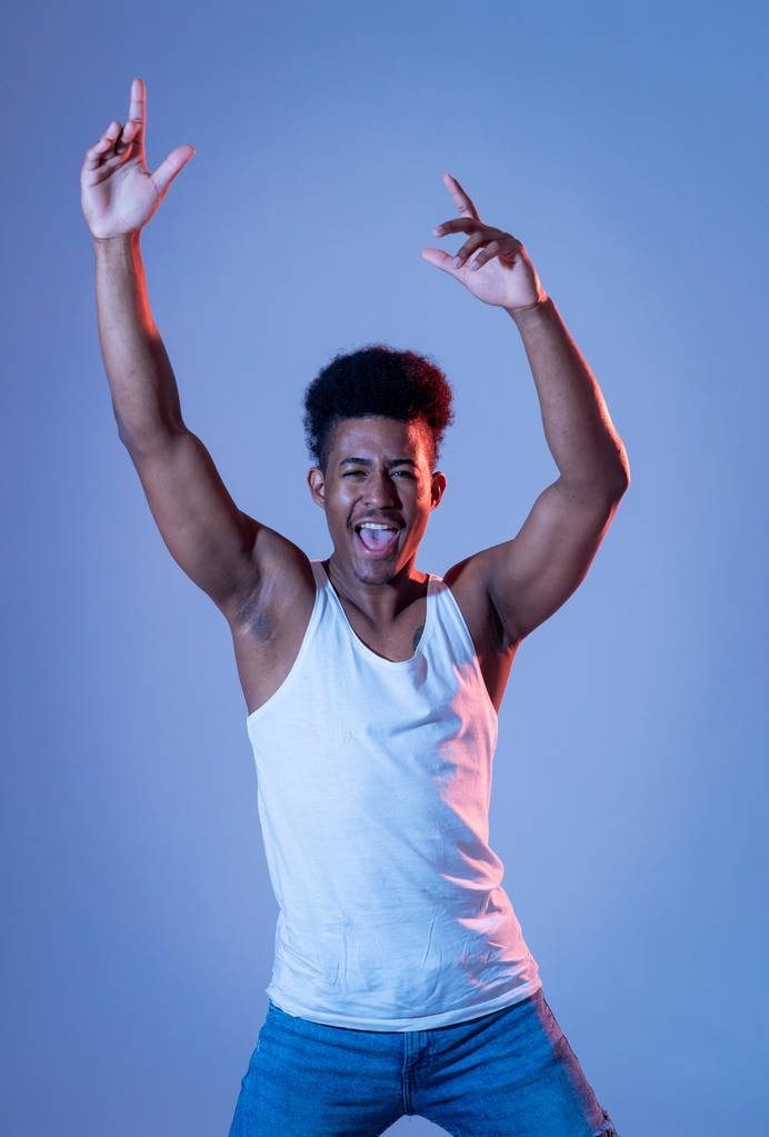 Portret van geïnspireerd cool African American tiener man dansen voelen de muziek en genieten van het leven op blauwe Moody Disco Neon lichte achtergrond. In mensen, jeugd feestnacht leven. Studio schot. - Foto, afbeelding