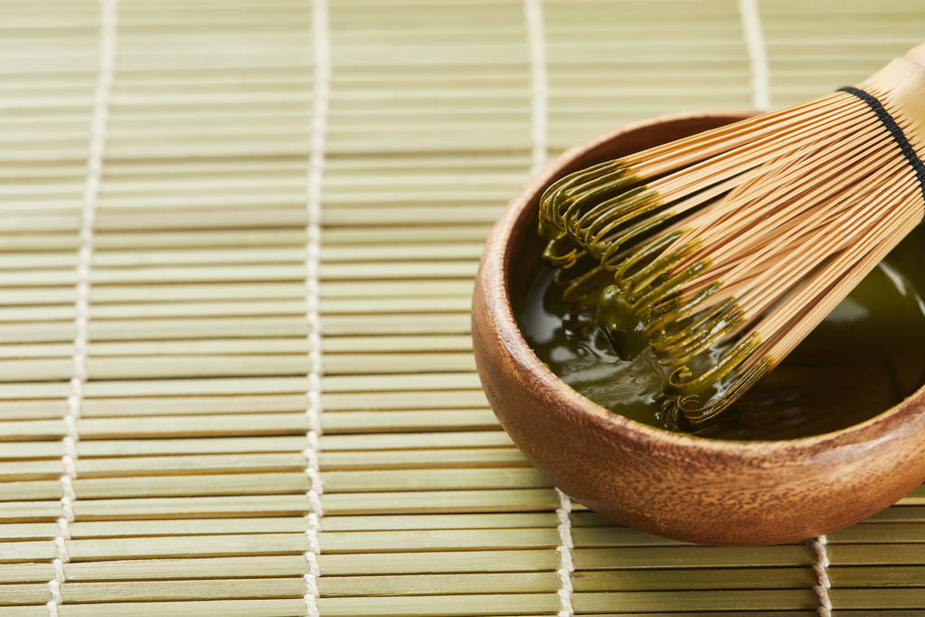 green matcha powder and bamboo whisk in wooden bowl on table mat with copy space - Photo, Image