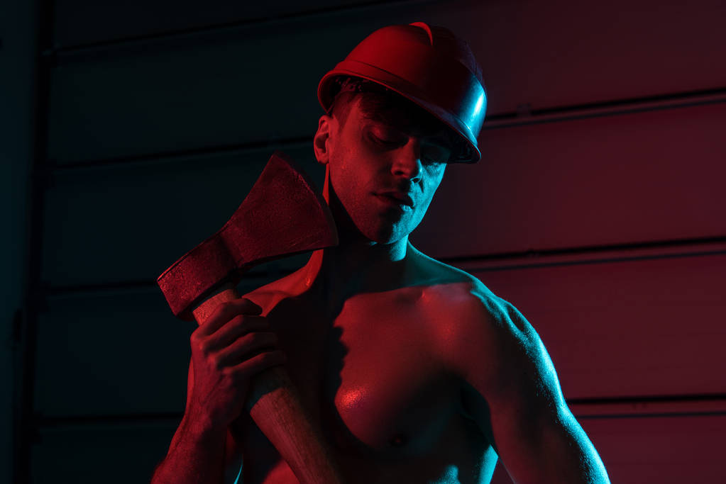 sexy shirtless fireman in protective helmet holding flat head axe in darkness - Photo, Image