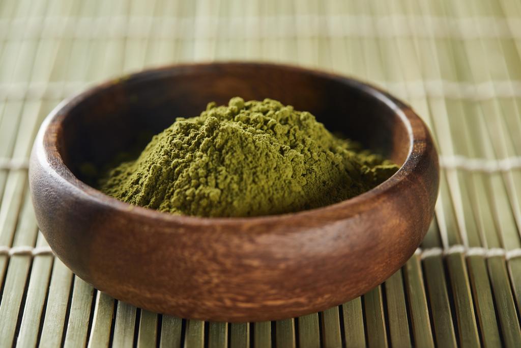 selective focus of green matcha powder in wooden bowl on bamboo table mat - Photo, Image