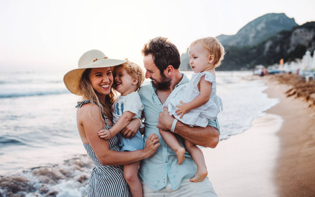 Une jeune famille avec deux enfants en bas âge debout sur la plage pendant les vacances d'été
. - Photo, image
