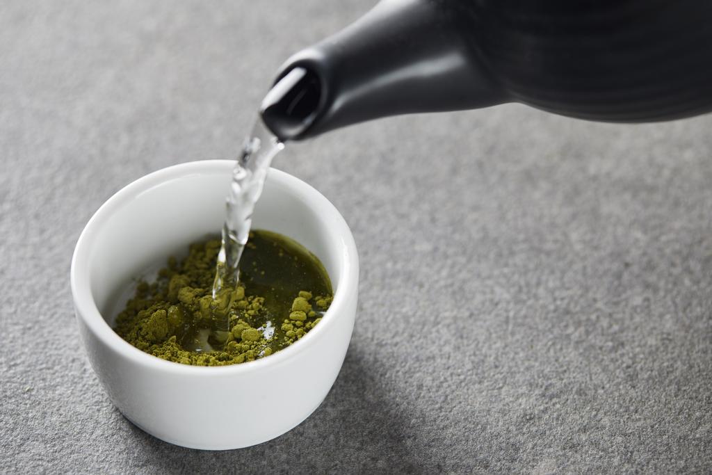 černý čajník nalévá vodu v bílém šálku se zeleným práškem na matča - Fotografie, Obrázek