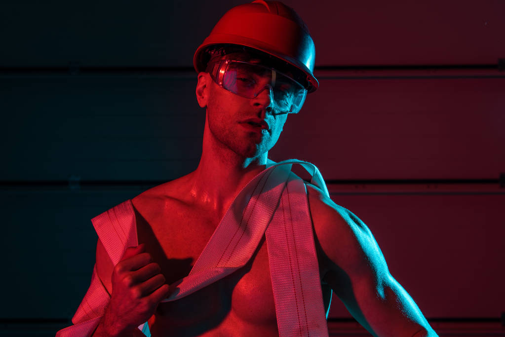 sexy caminetto senza camicia in casco protettivo che tiene il tubo del fuoco nel buio
 - Foto, immagini