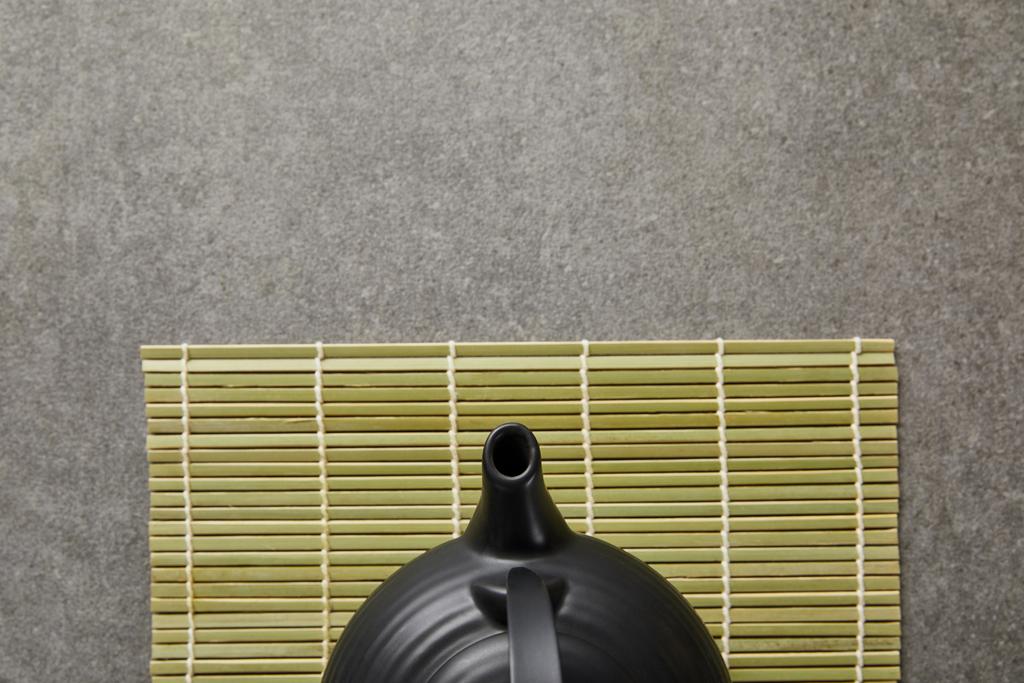 Ansicht der grünen Bambus-Tischmatte mit schwarzer Teekanne auf grauer Oberfläche - Foto, Bild