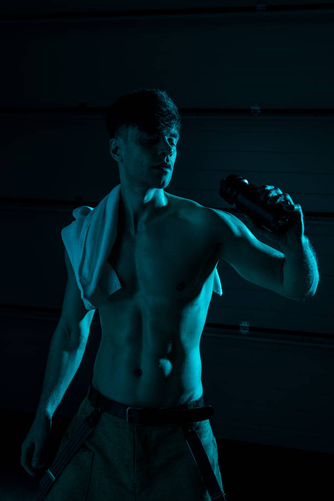 sexy shirtless man with towel holding sport bottle in darkness - Photo, Image