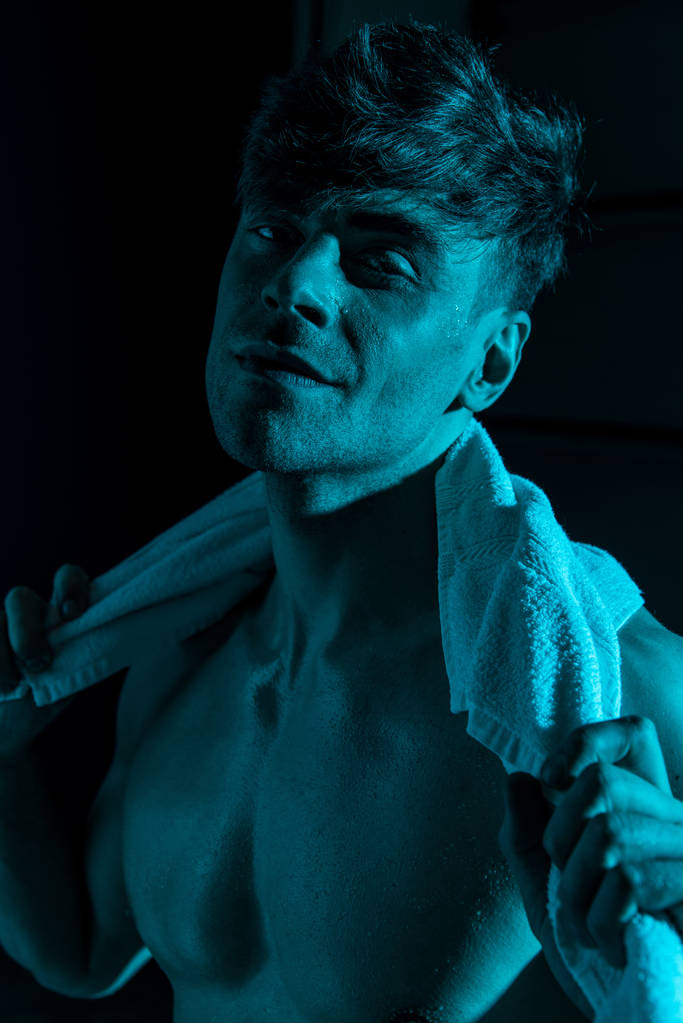 usměvavý sexy muž s ručníkem na kameru v temnotě - Fotografie, Obrázek
