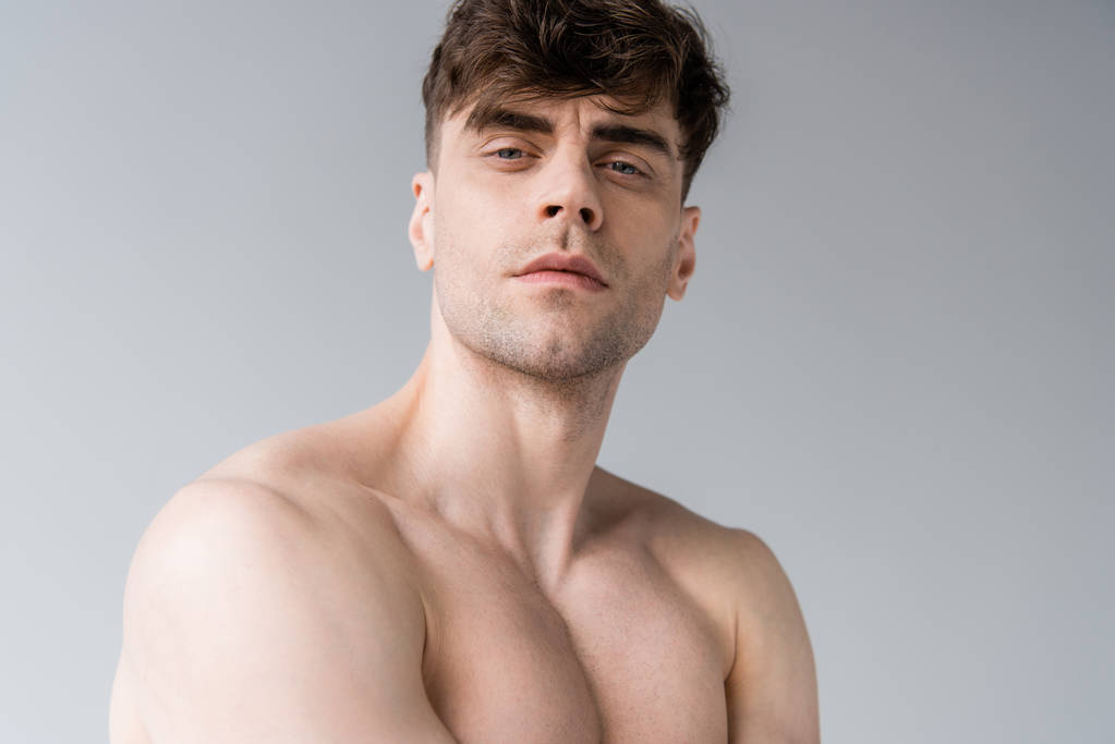 серьезный сексуальный мускулистый мужчина без рубашки, смотрящий на камеру, изолированную на сером
 - Фото, изображение