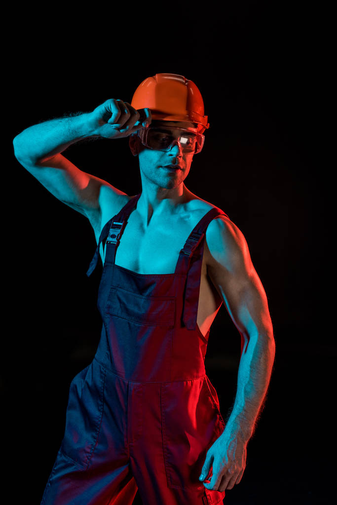 sexy fireman in overall, hardhat and protective goggles isolated on black - Photo, Image