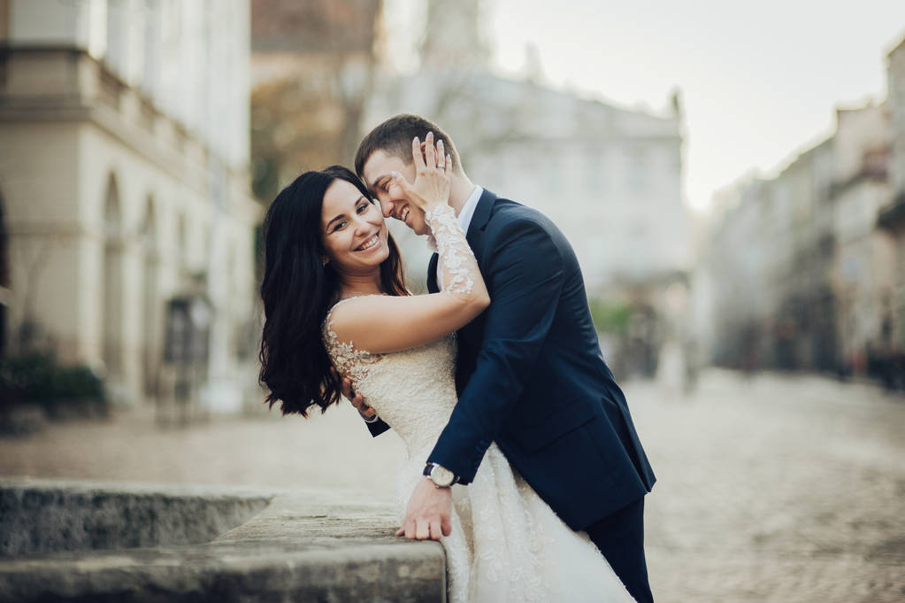 Ευτυχισμένος γαμπρός και κομψή νύφη σε δαντέλα νυφικό που ποζάρει στο δρόμο της πόλης  - Φωτογραφία, εικόνα