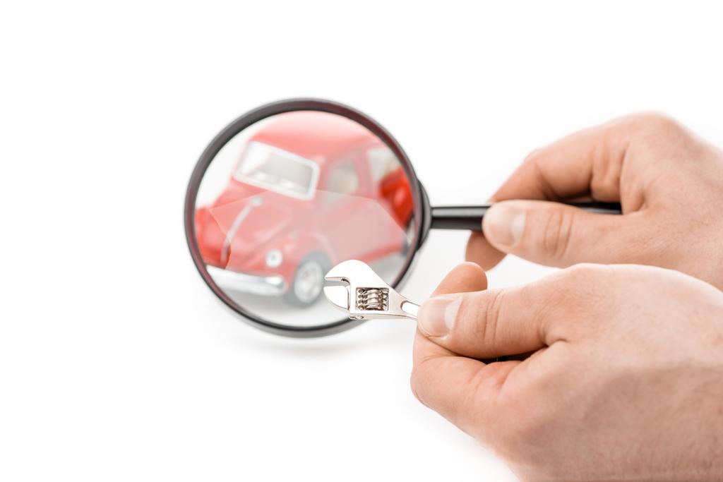 Ausgeschnittene Ansicht eines Mannes mit Lupe und Schraubenschlüssel vor Spielzeugauto isoliert auf weiß - Foto, Bild