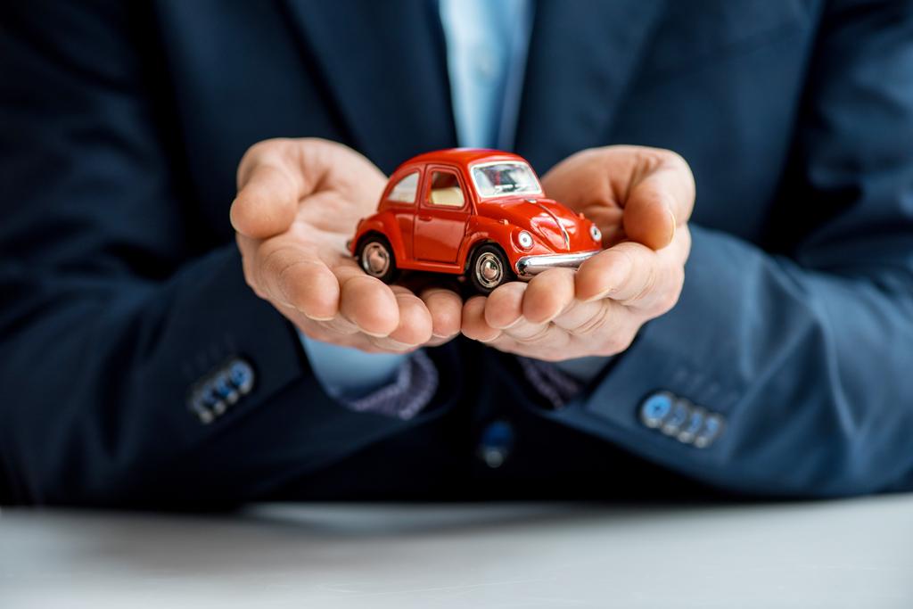 μερική θέα του ανθρώπου σε επίσημη φθορά κρατώντας κόκκινο παιχνίδι αυτοκίνητο - Φωτογραφία, εικόνα