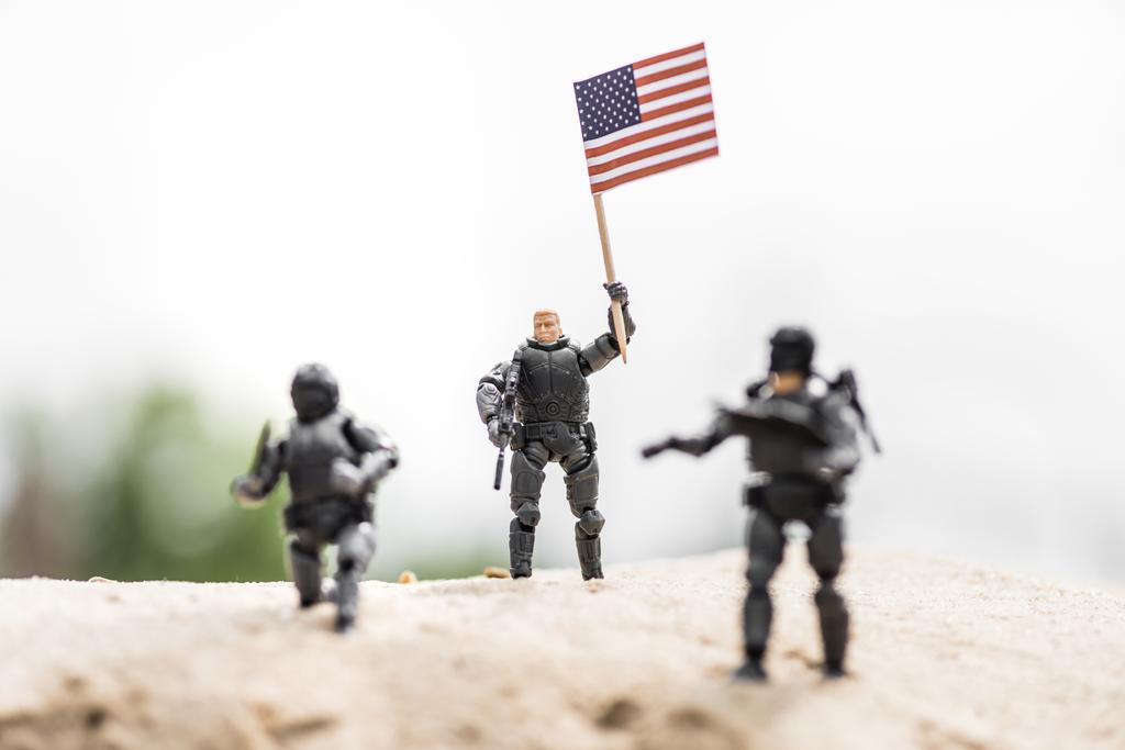 selective focus of toy soldier with weapon holding american flag on sand - Photo, Image