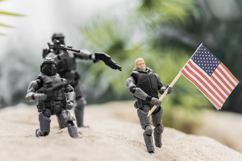 selektywne skupienie żołnierzy zabawek mających na broń na zabawkę z amerykańską flagą na piasku wzgórza - Zdjęcie, obraz