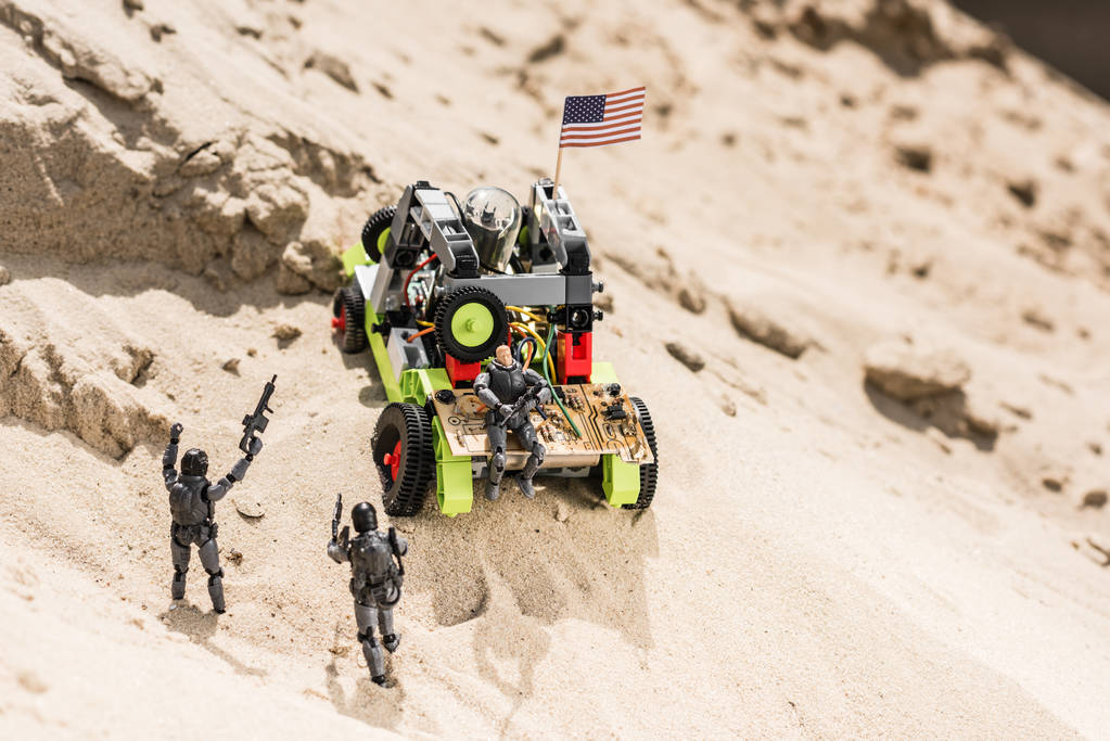 plastic speelgoed soldaten op zandduin in de buurt van auto met Amerikaanse vlag - Foto, afbeelding