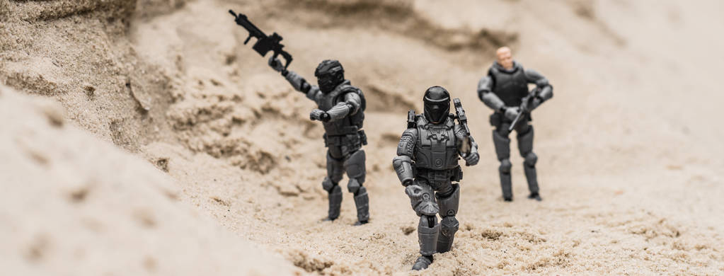 selektivní zaměření plastických vojáčků na písečné duny se zbraněmi, panoramatickým výstřesem - Fotografie, Obrázek