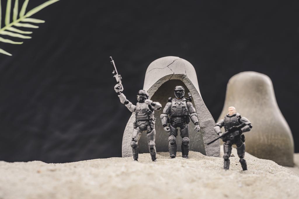 Zabawka żołnierzy z bronią i amerykańskiej flagi stoi w pobliżu jaskiń na wydmach piasku na czarnym tle - Zdjęcie, obraz