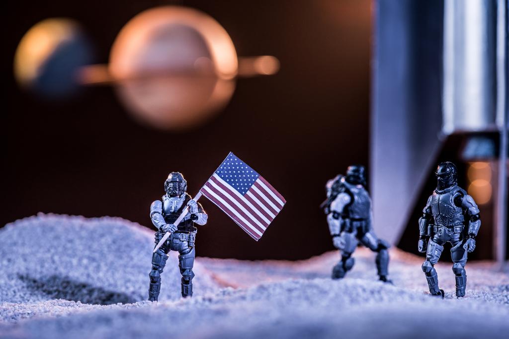 selective focus of toy astronauts holding american flag in space near rocket - Photo, Image