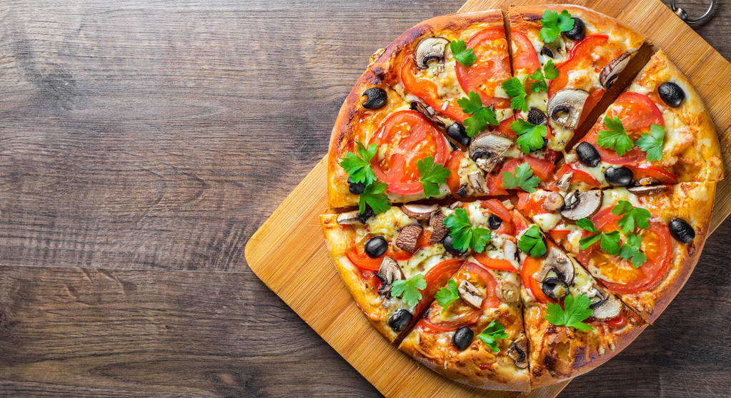 szeletelt pizza mozzarella sajttal, paradicsommal, borssal, olíva, gomba, fűszerek és friss levél. Olasz pizza a fából készült asztal háttereként - Fotó, kép