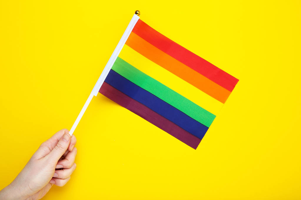 Female hand holding rainbow flag on yellow background - Photo, Image