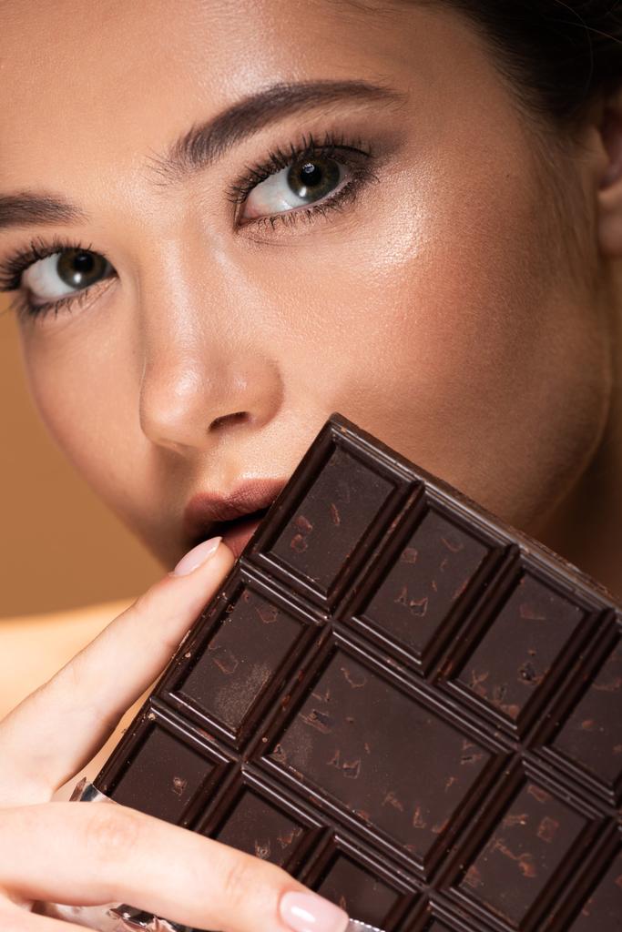 όμορφη νεαρή γυναίκα κρατώντας μπάρα σοκολάτας απομονωμένη σε μπεζ - Φωτογραφία, εικόνα