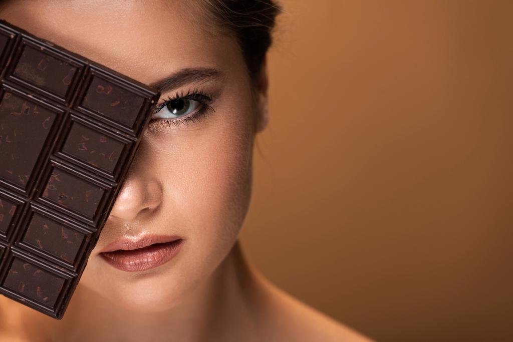 beautiful young woman with obscure face holding chocolate bar isolated on beige - Photo, Image