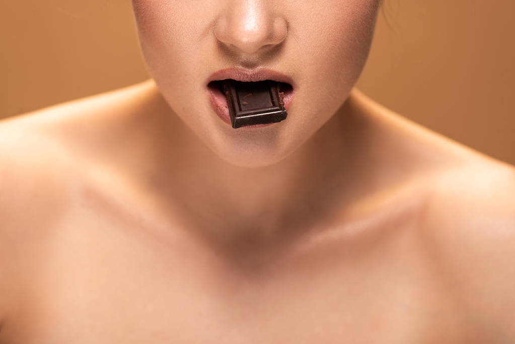 ベージュに隔離されたチョコレート片を食べるヌード若い女性のトリミングされたビュー  - 写真・画像