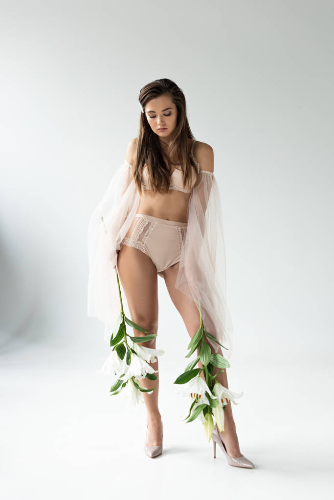tendre jeune femme en lingerie beige et manches en mesh tenant des lys sur blanc
 - Photo, image