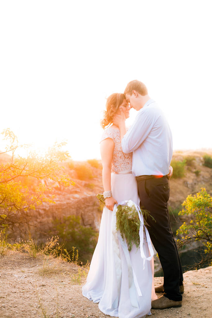 Elegant gentle stylish groom and bride near river or lake on sunset in summer. Wedding couple in love  - Photo, Image