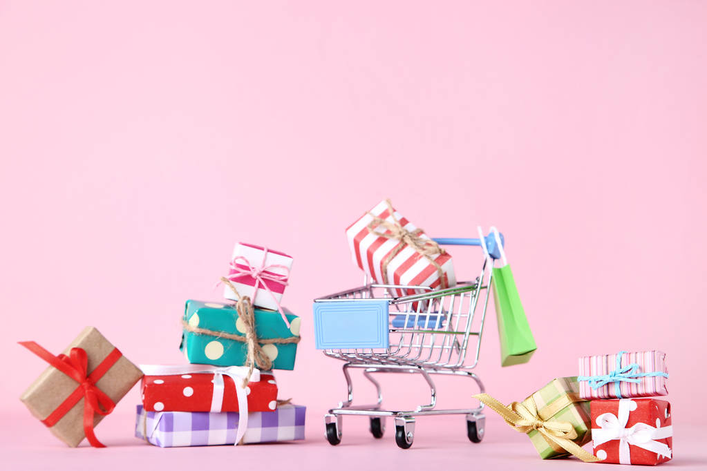 Pequeño carrito de compras con cajas de regalo sobre fondo rosa
 - Foto, imagen