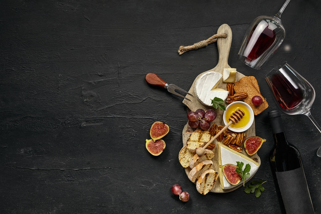 Due bicchieri di vino rosso e piatto di formaggio con frutta sulla pietra nera
 - Foto, immagini