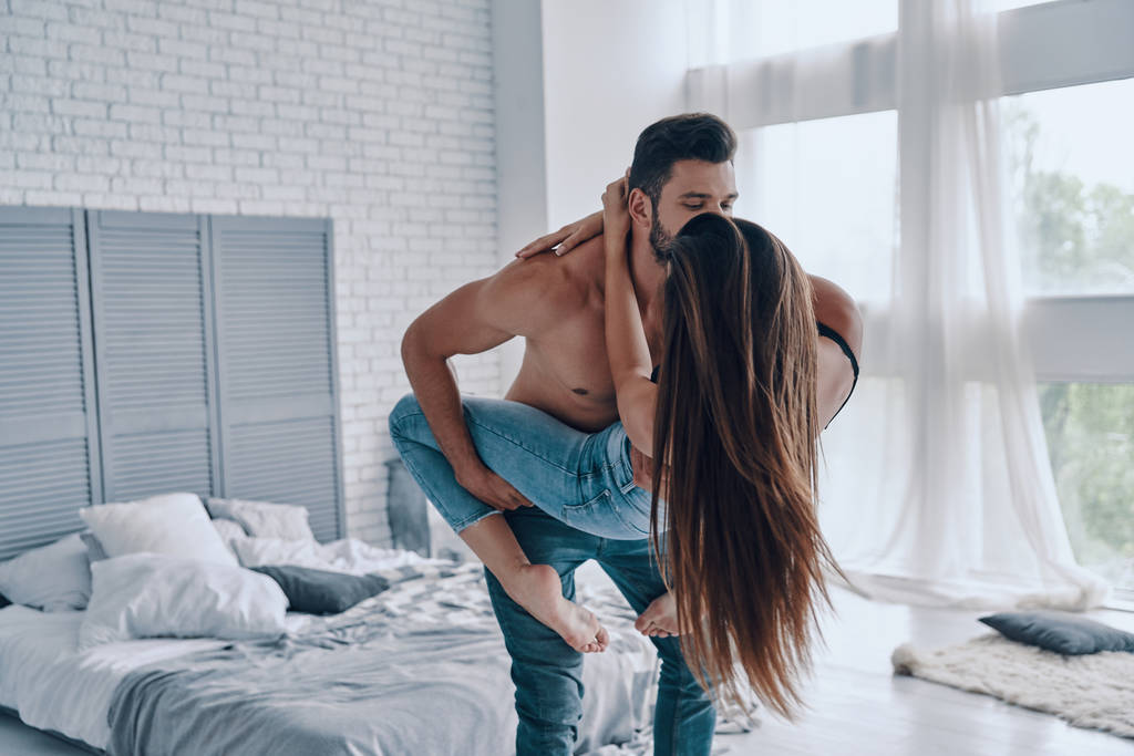 heureux beau jeune couple embrassant tout debout face à face dans chambre à coucher, homme embrassant femme
  - Photo, image