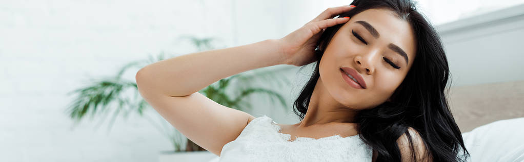 panoramic shot of happy asian girl with closed eyes touching hair  - Photo, Image