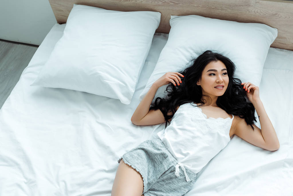 εναέρια θέα της χαρούμενο ασιατικό κορίτσι που κείτεται στο κρεβάτι  - Φωτογραφία, εικόνα