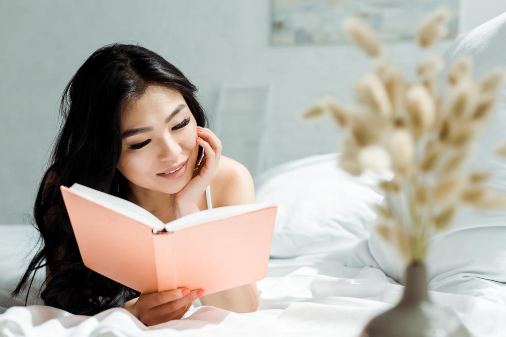 foyer sélectif de positive asiatique fille lecture livre tout allongé sur lit à la maison
  - Photo, image