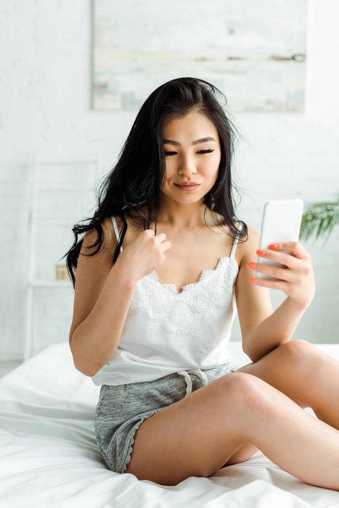 selectieve focus van mooi Aziatisch meisje met behulp van smartphone in de slaapkamer  - Foto, afbeelding