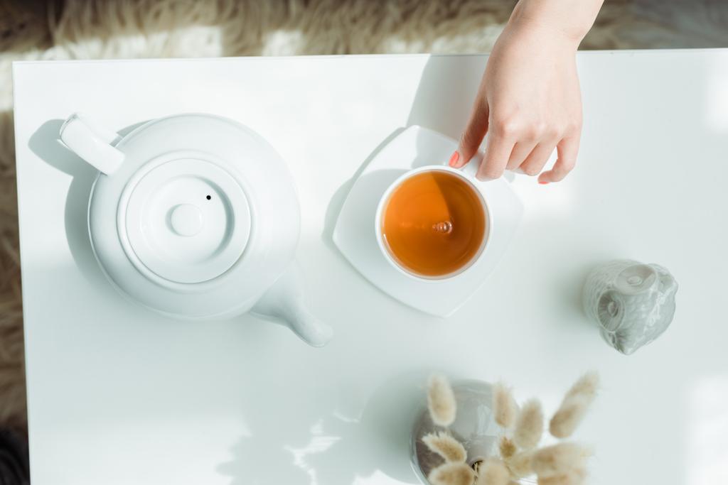 vista ritagliata della donna in possesso di tazza con tè vicino teiera e vaso con rami di salice
  - Foto, immagini