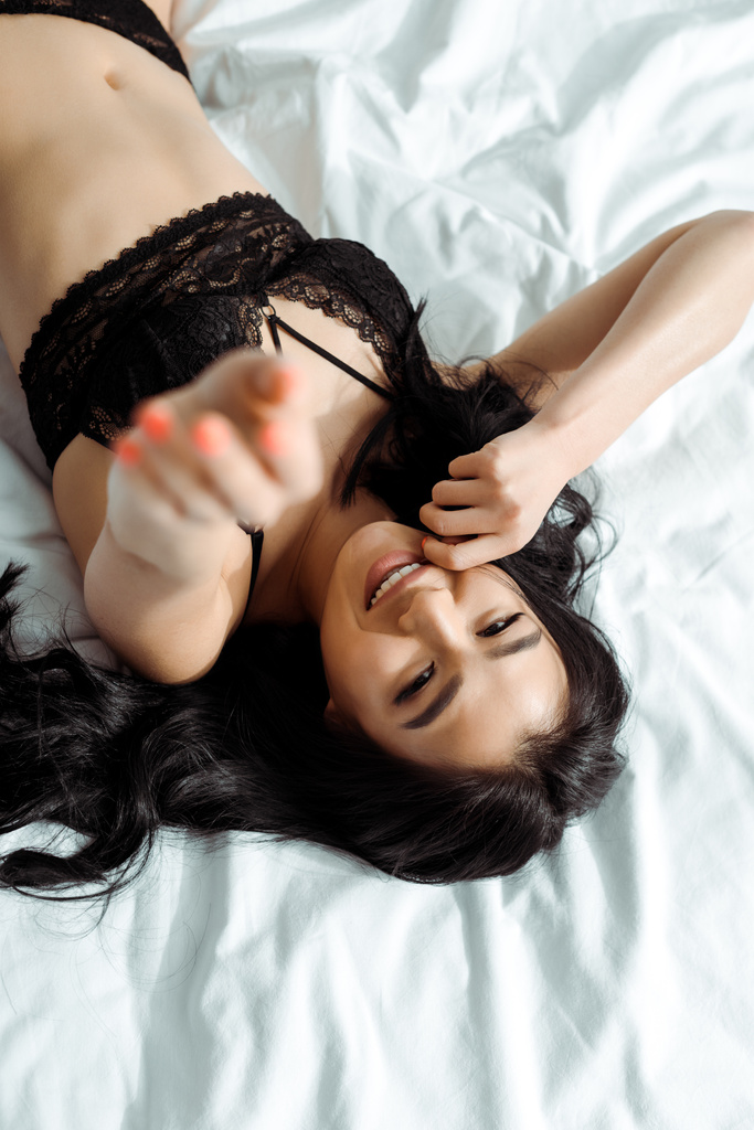 enfoque selectivo de la mujer tailandesa feliz en ropa interior negro acostado en la cama
  - Foto, imagen