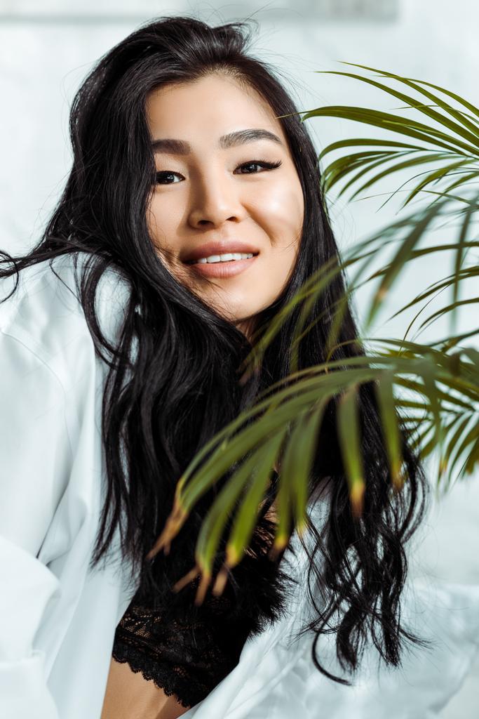 selective focus of happy asian woman looking at camera near plant  - Photo, Image