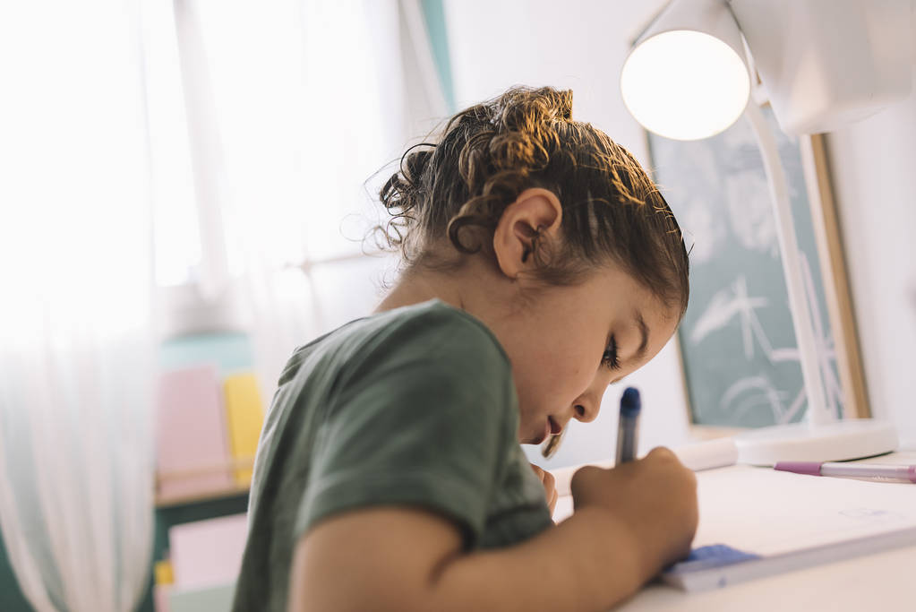 Маленькая девочка рисует сосредоточенно в своем столе
 - Фото, изображение