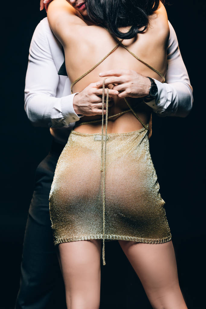 обрезанный вид мужчины раздевается сексуальная молодая женщина в золотом прозрачном платье изолированы на черном
 - Фото, изображение