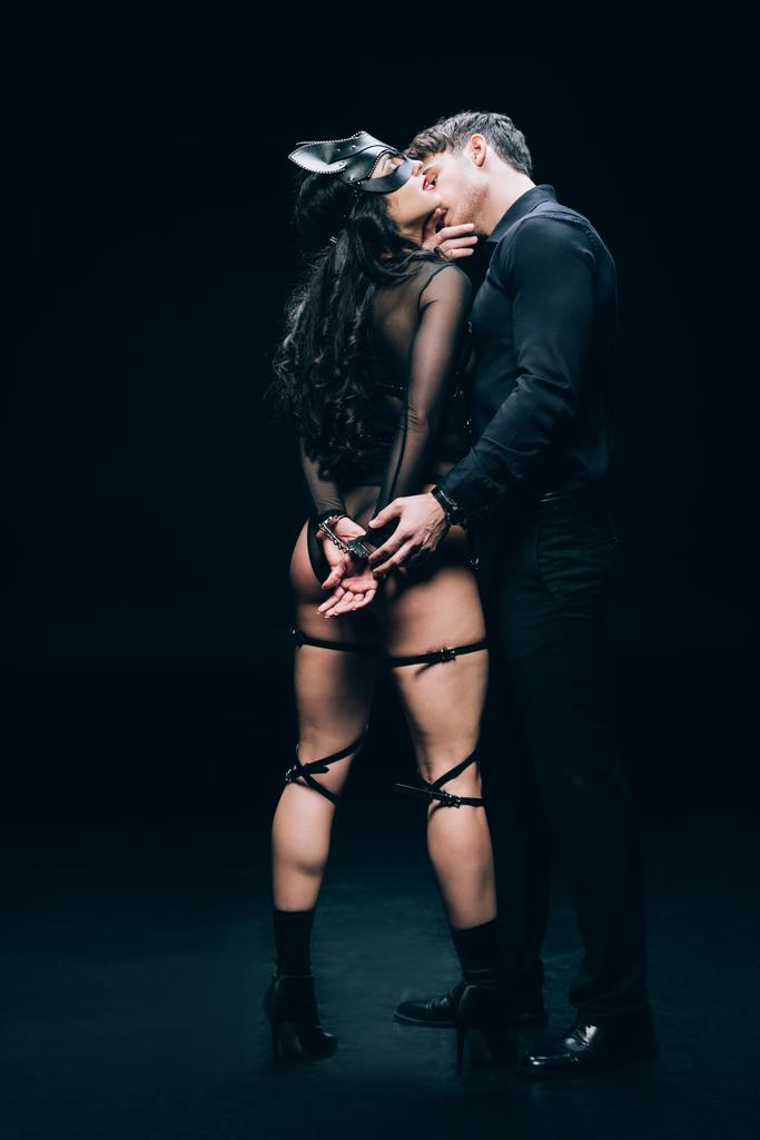 Mann küsst sexy Frau in Handschellen und sexy bdsm Kostüm auf schwarzem Hintergrund - Foto, Bild