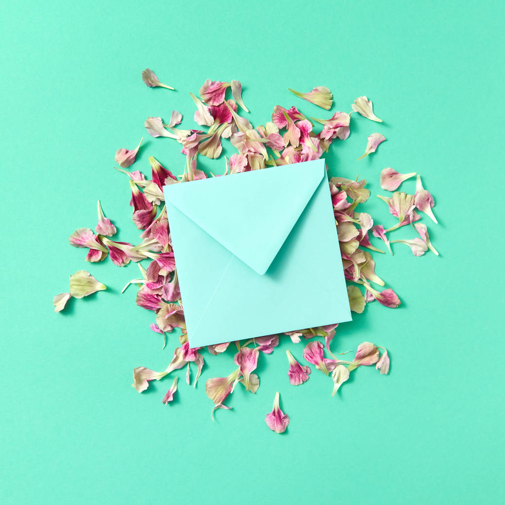 Carte de voeux avec enveloppe faite à la main sur des pétales de fleurs sur un fond turquoise et espace de copie. Pose plate. Maquette
. - Photo, image