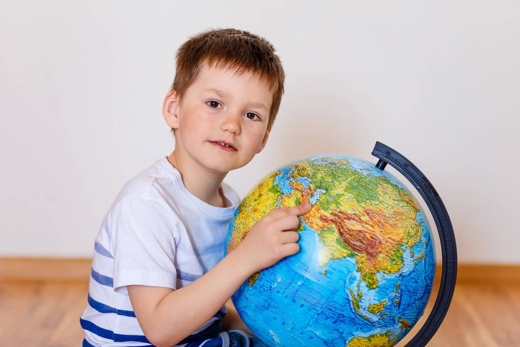Симпатичный пятилетний ребенок показывает палец страны на большом глобусе
 - Фото, изображение