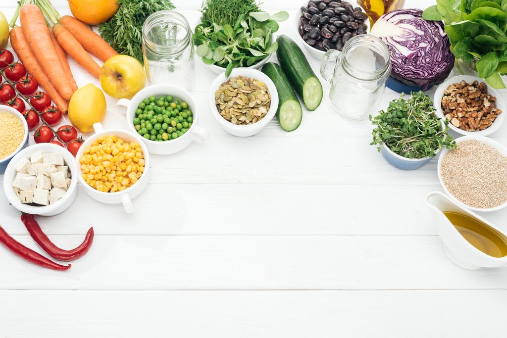 vista superior de frutas e legumes orgânicos perto de frascos de vidro na mesa branca de madeira com espaço de cópia
 - Foto, Imagem