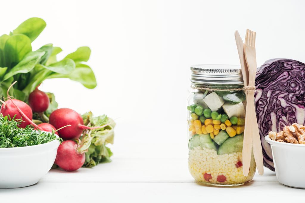salade de légumes frais dans un bocal en verre près de radis, chou rouge et noix isolé sur blanc
 - Photo, image