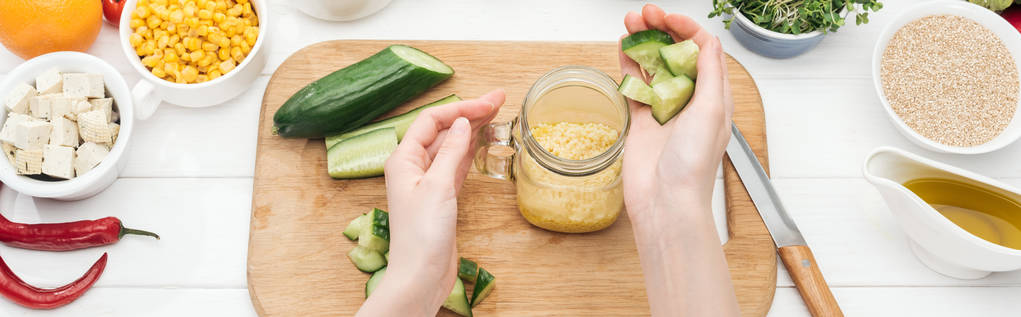 bijgesneden beeld van de vrouw het toevoegen van gehakte komkommer aan couscous in glazen pot op houten snijplank, panoramische schot - Foto, afbeelding